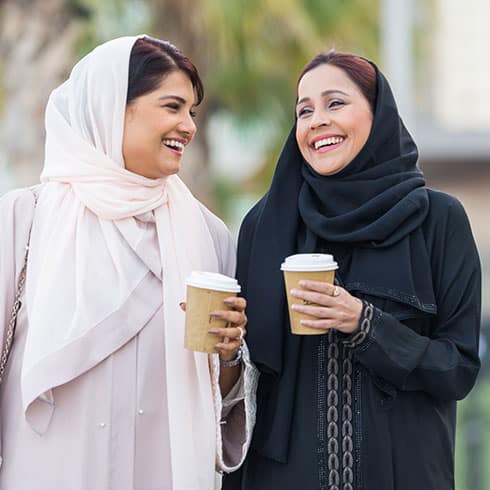 two women walk drinking coffee and laughing