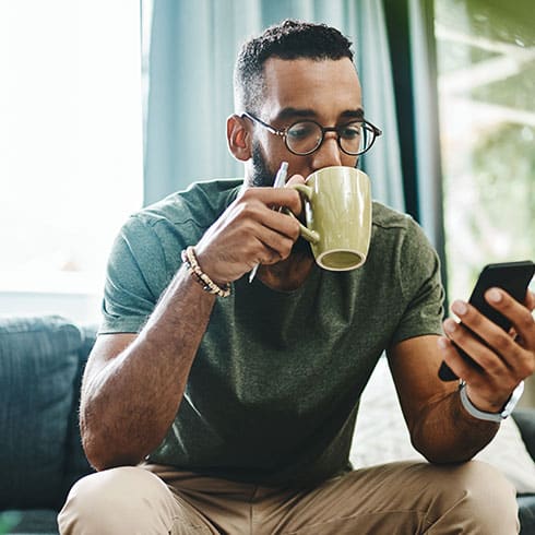 a man sits drinking from a mug looking at his phone