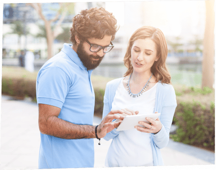 two people stand outside looking at a tablet